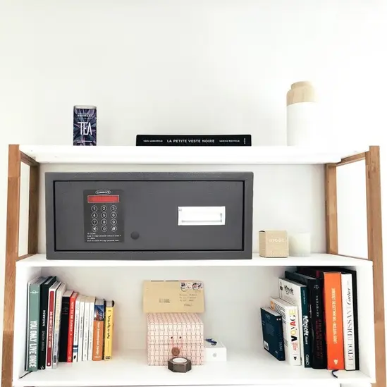 Метален сейф UNS  MT1 - разположен на секция, редом с книги, затворен, черен